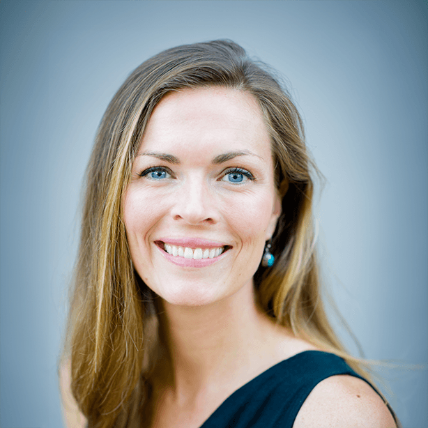 Smiling woman with long, light brown hair, wearing a black top and turquoise earrings against a soft, blurred background.