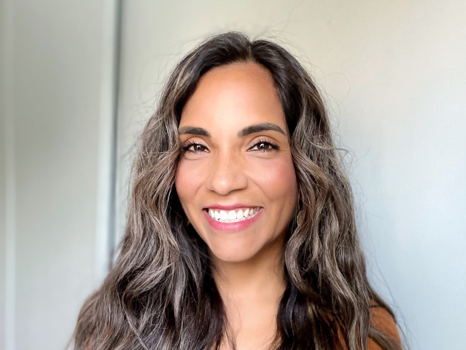 Smiling woman with long, wavy hair against a plain background.